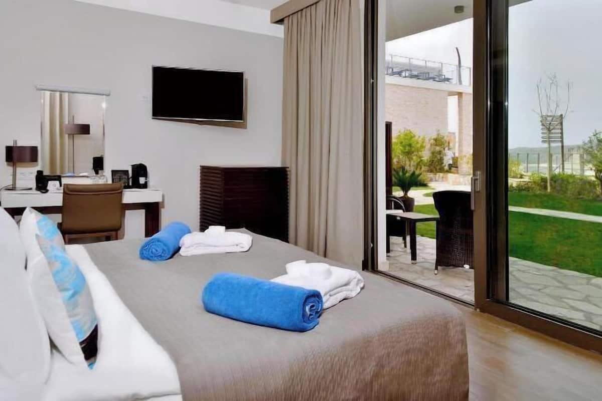 A hotel room with a bed, a desk, a chair, a TV, and a view of the outdoors.