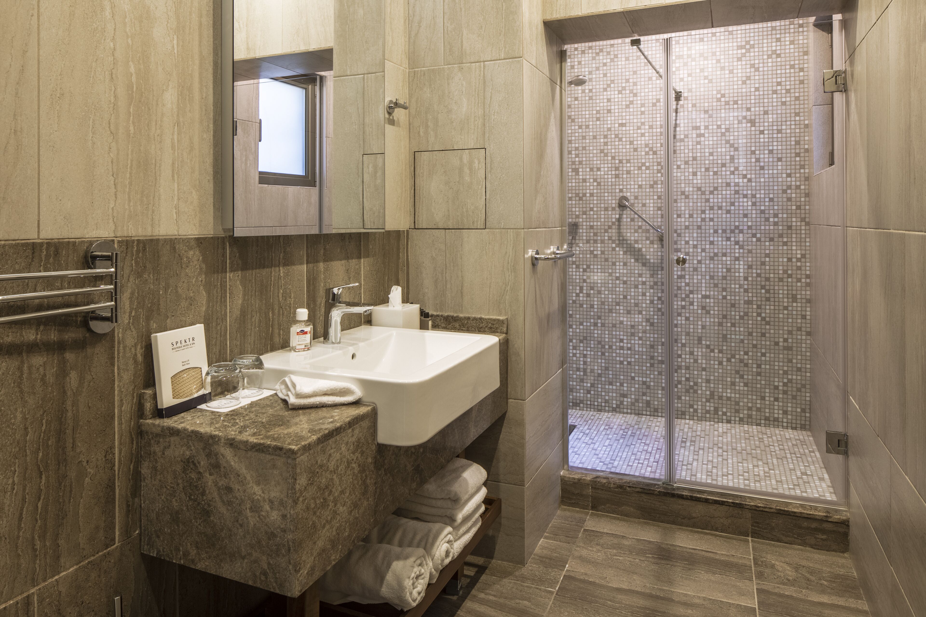 Un baño moderno con lavamanos de mármol, cabina de ducha con mampara de vidrio y un perchero para toallas.