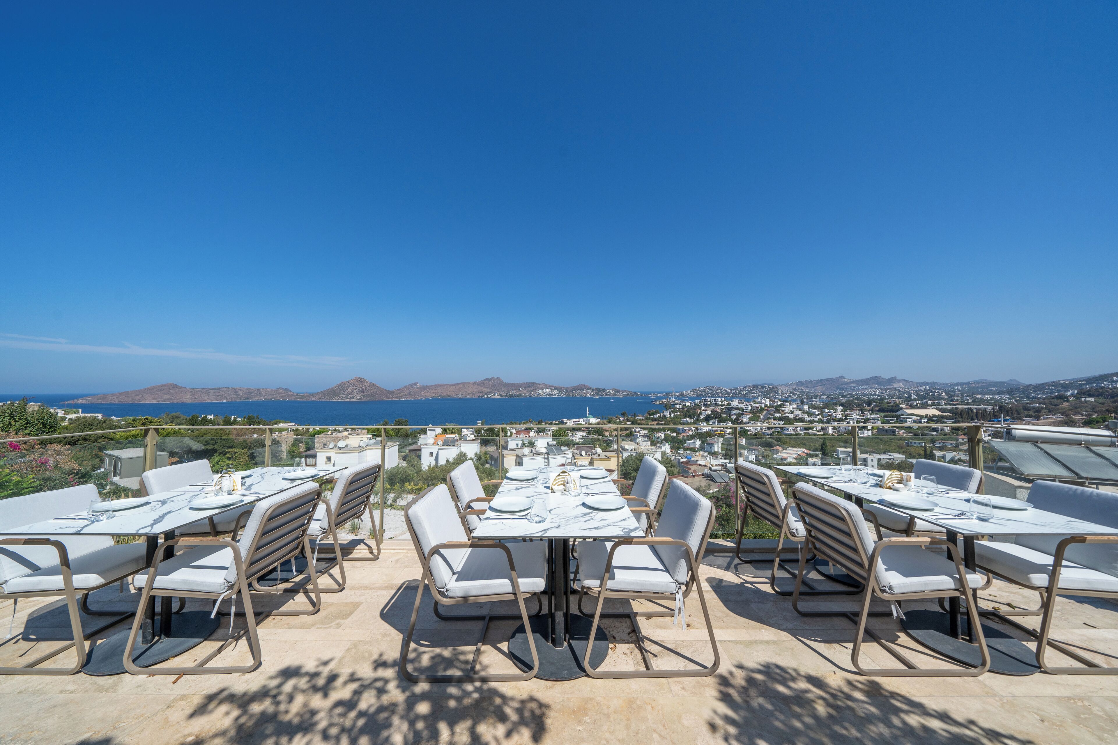 An outdoor dining area with a table set for six, overlooking a scenic view of the sea and distant mountains.