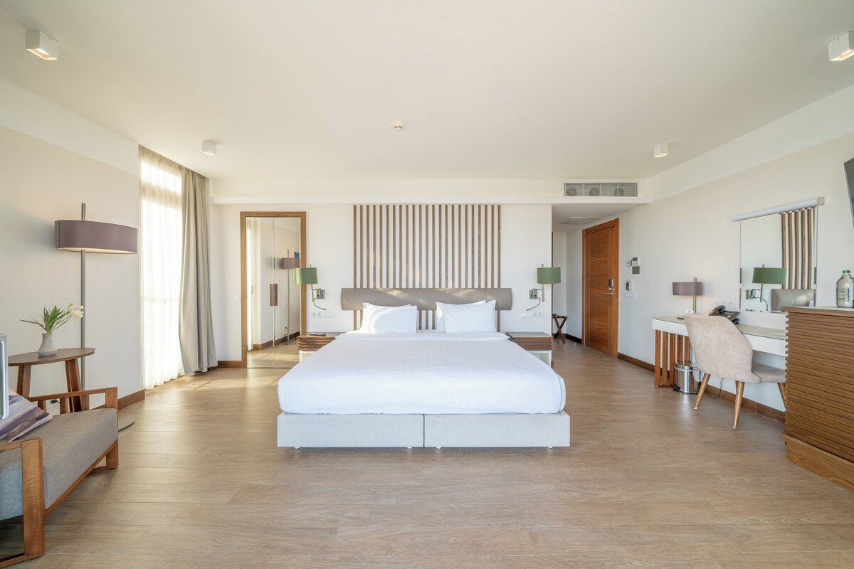 A spacious hotel room with a large bed, a desk, and a chair.