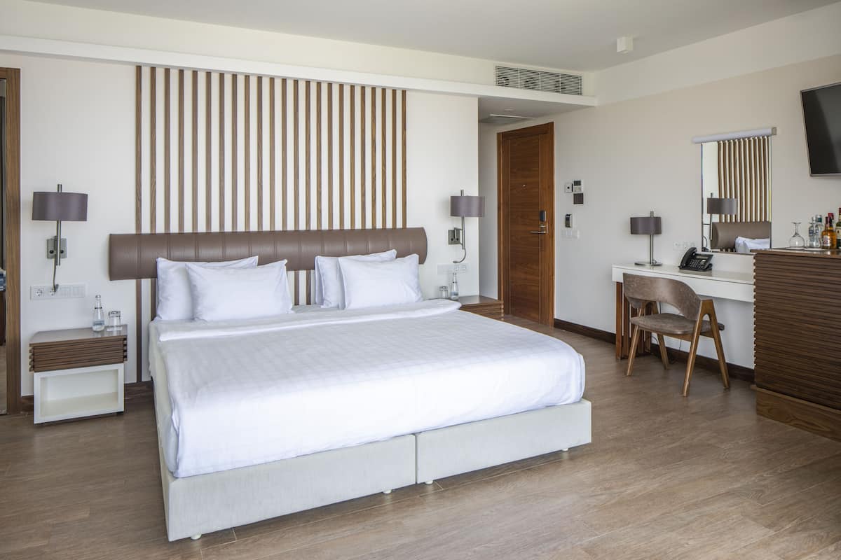 A modern hotel room with a large bed, bedside tables, a desk, and a chair.