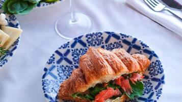Mesa posta com diversos pratos, incluindo um croissant, salada e um copo de bebida vermelha.