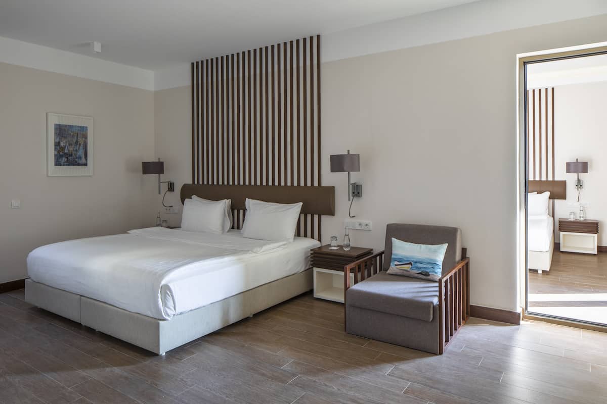 A modern hotel room with a large bed, bedside tables, a chair, and a view through a glass door.