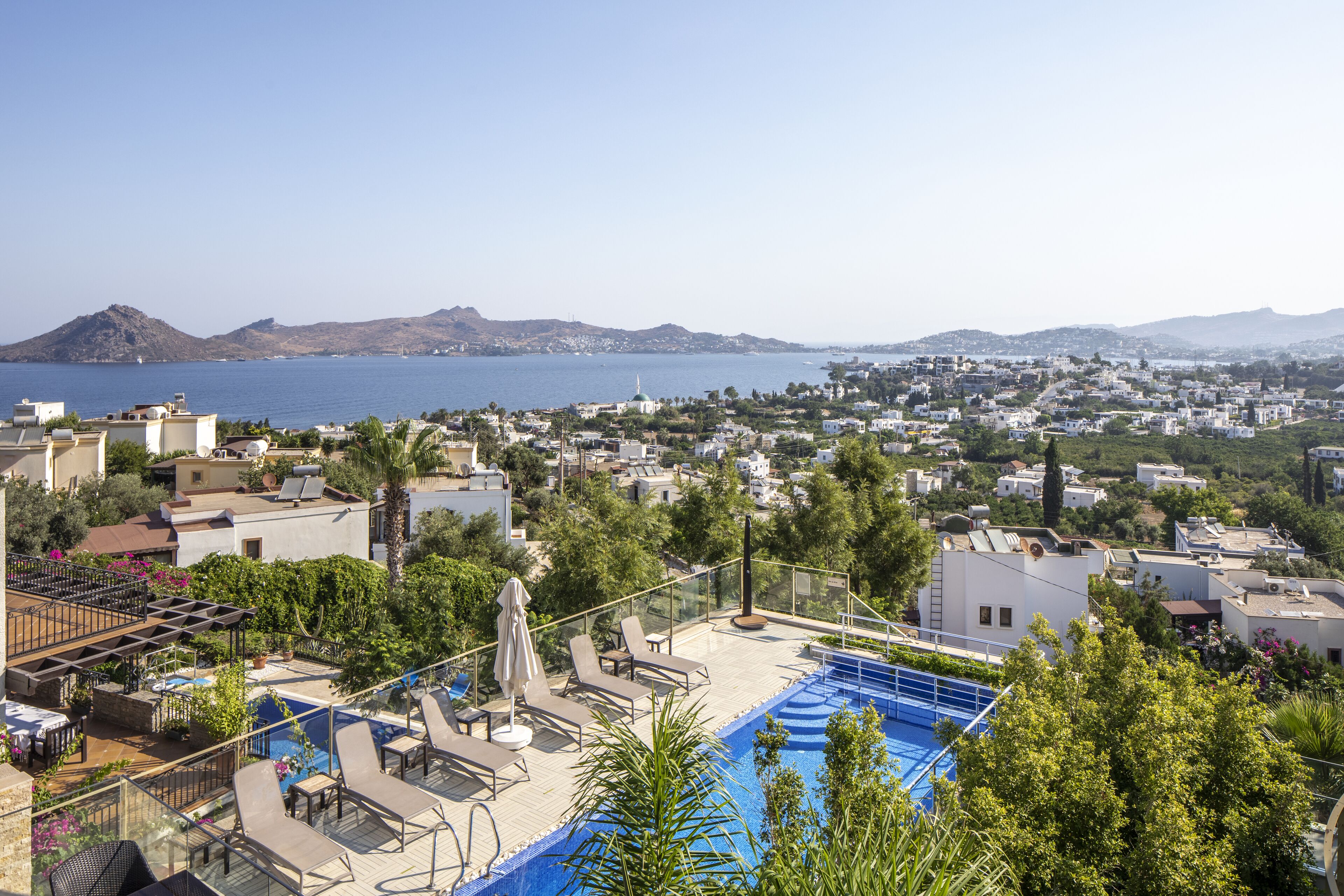 A rooftop pool area with lounge chairs and a view of the sea and cityscape.