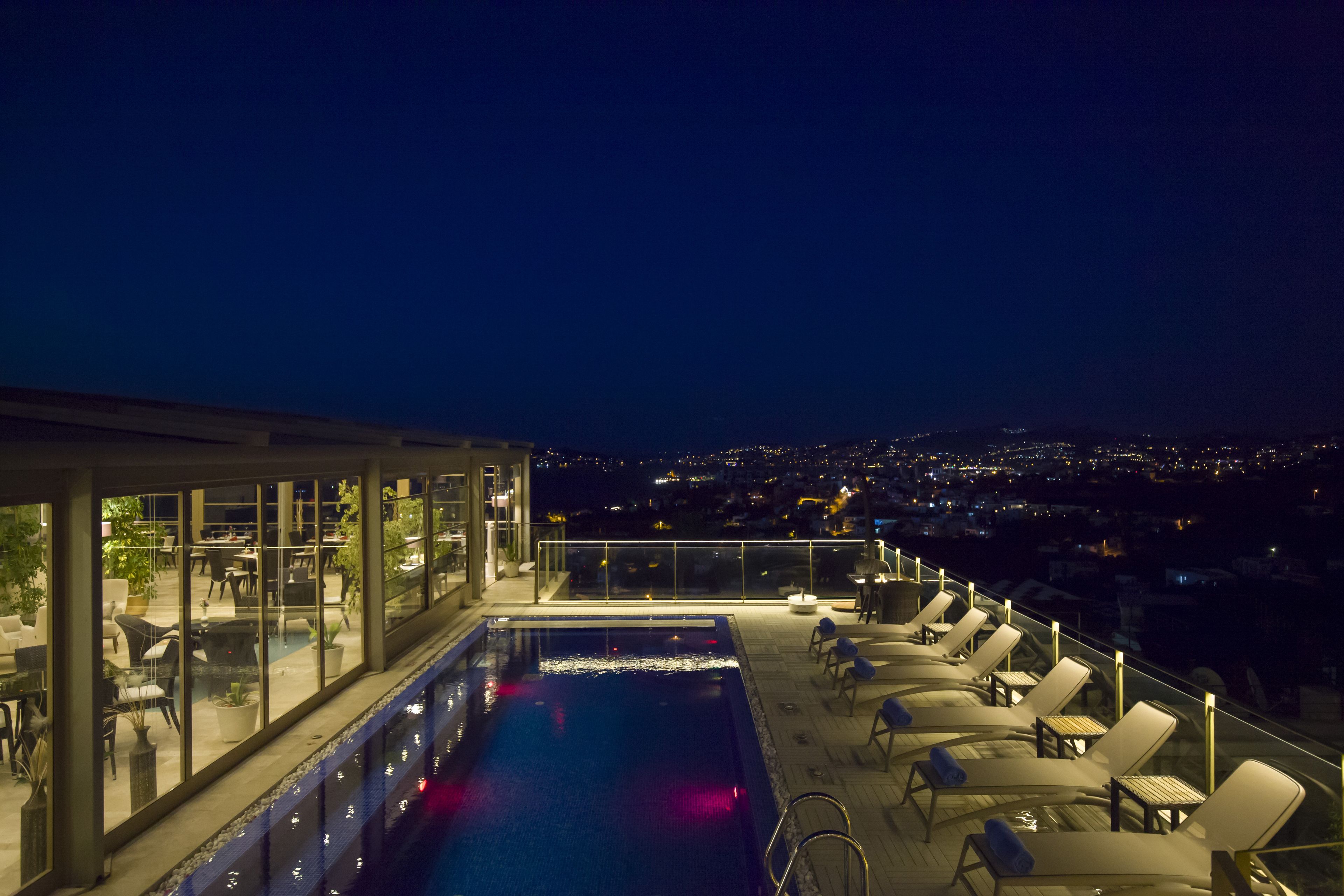 Ein Poolbereich auf dem Dach mit Liegestühlen und Blick auf die nächtliche Stadt.