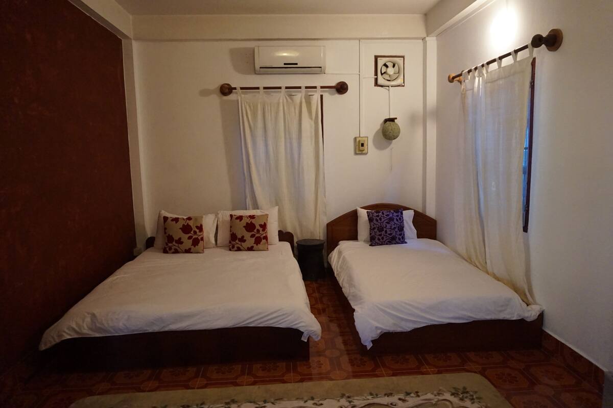 A room with two single beds, a ceiling fan, an air conditioning unit, and a small wall-mounted decoration.