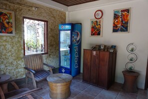 A room with a wooden chair, a woven basket, a blue Pepsi refrigerator, a wooden cabinet, and two wall paintings.
