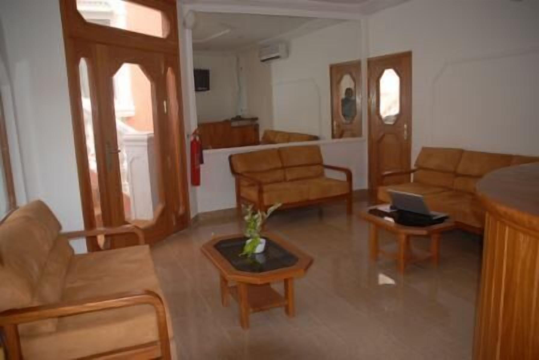Uma sala de estar com móveis de madeira, uma mesa de centro com um vaso e um laptop sobre uma mesinha lateral.