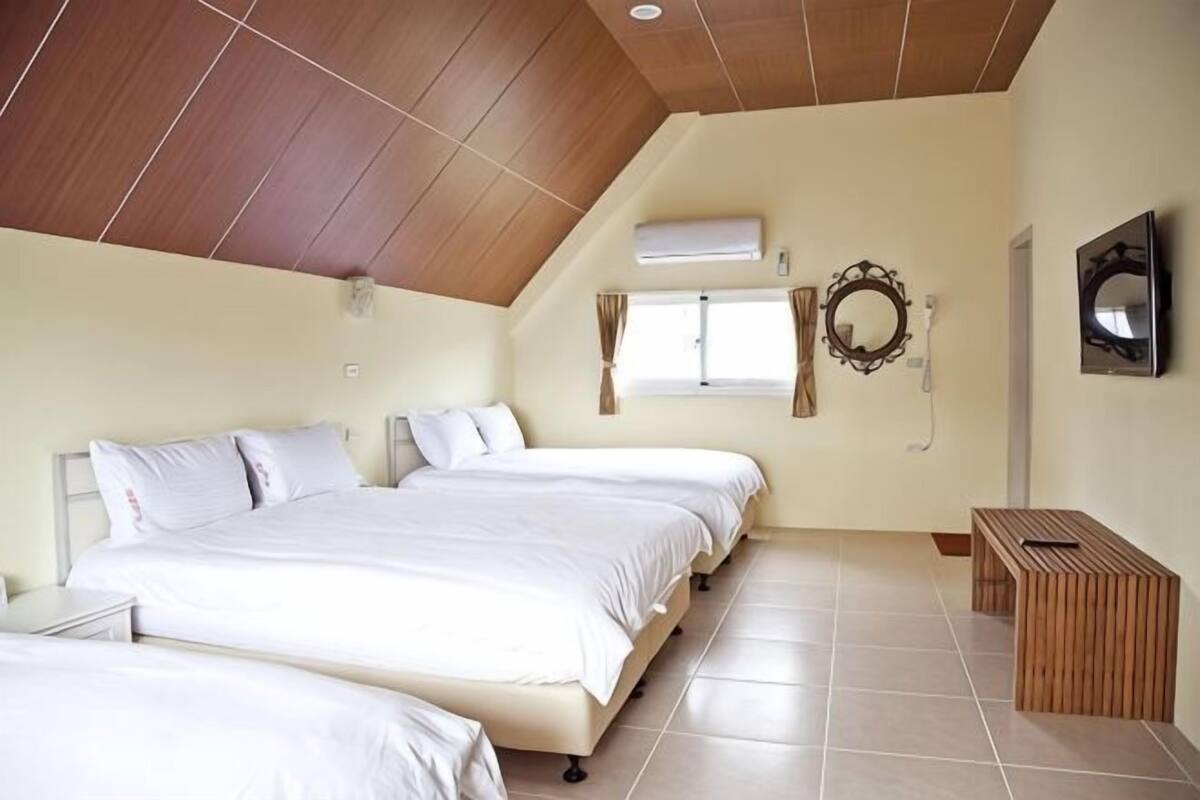 A bedroom with two beds, a wooden ceiling, a window, a mirror, and a TV.