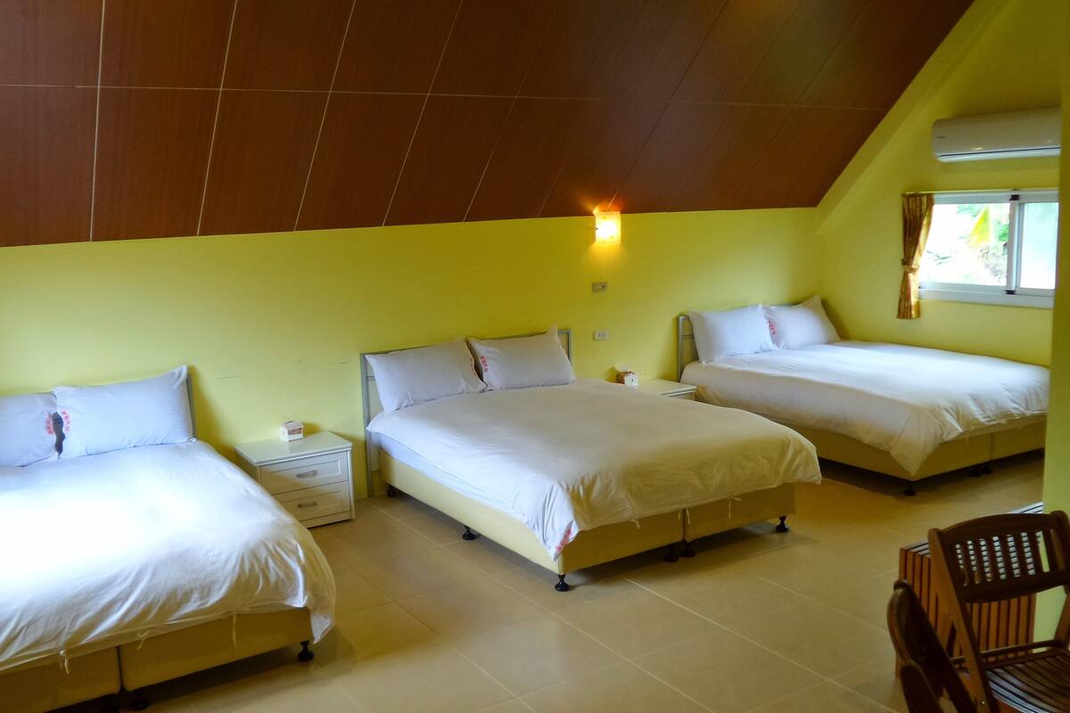 A room with three single beds, a wooden ceiling, and a window with curtains.