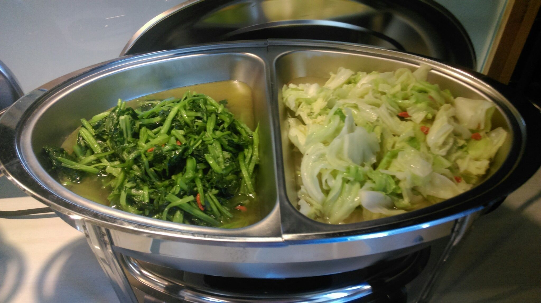 A stainless steel food container with two compartments, one containing green leafy vegetables and the other containing shredded cabbage.