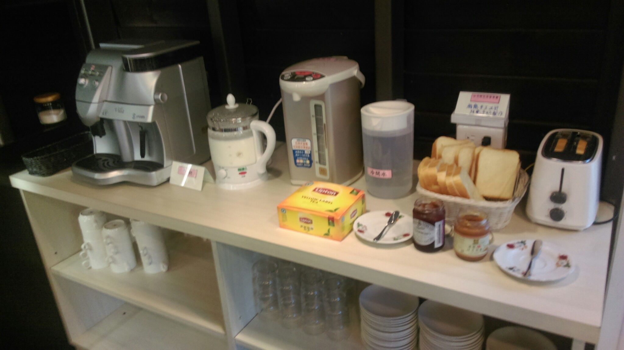 A breakfast bar with a coffee maker, a blender, a toaster, and various breakfast items like bread, jam, and a carton of milk.