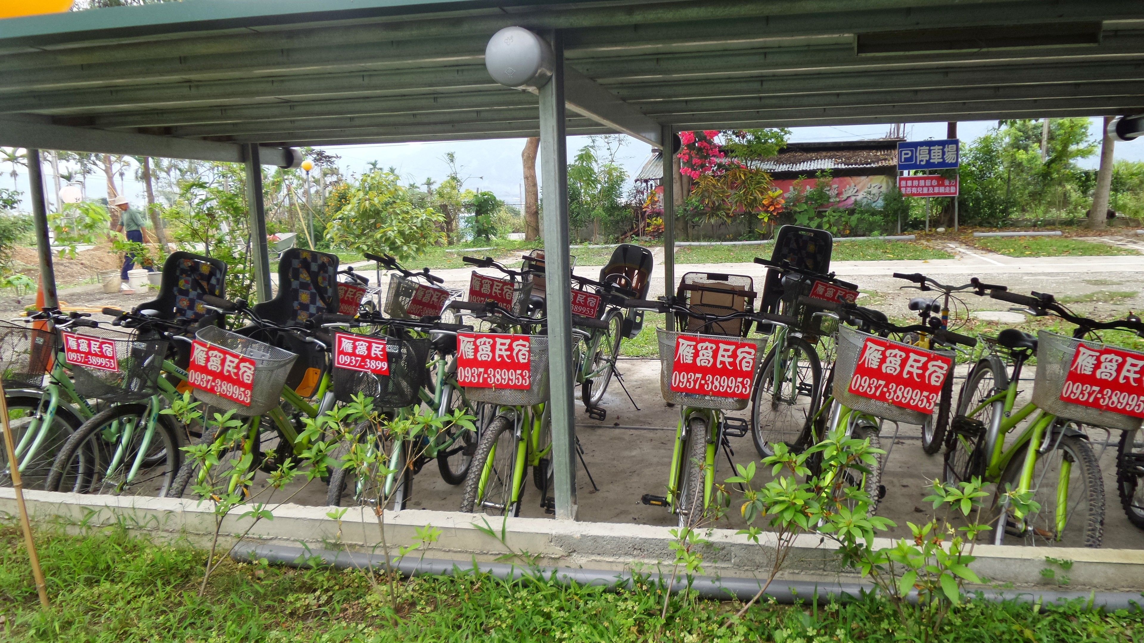 A covered bicycle parking area with multiple bicycles and red signs with contact numbers.