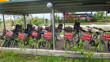 A covered bicycle parking area with multiple bicycles and red signs with contact numbers.