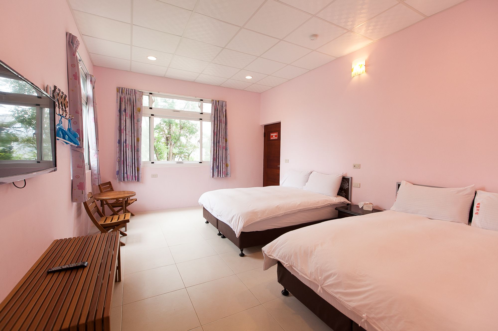 A bedroom with two beds, a wooden table, and a window with curtains.