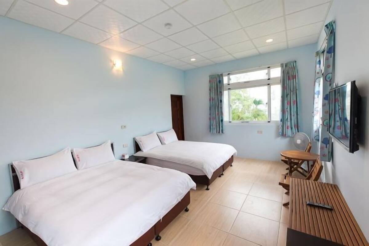 A hotel room with two beds, a wooden table, a TV, and a window with curtains.