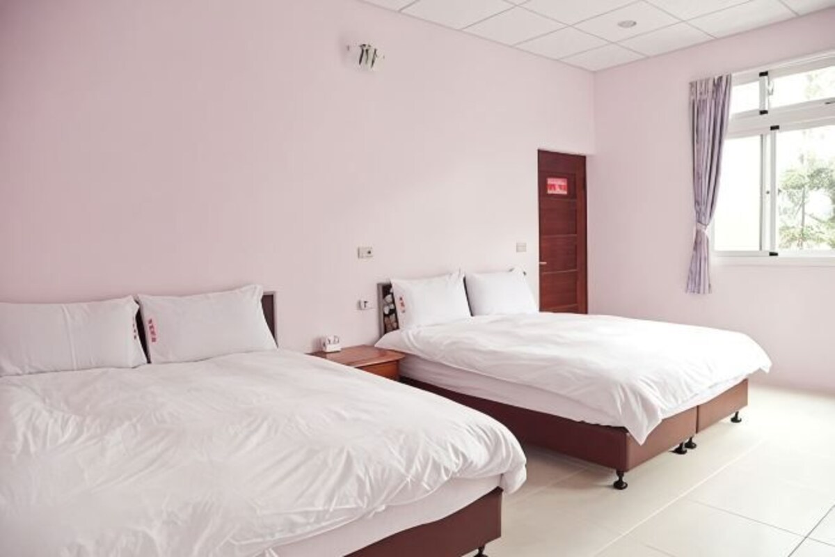 A hotel room with two beds, a wooden wardrobe, a window with curtains, and a ceiling light.