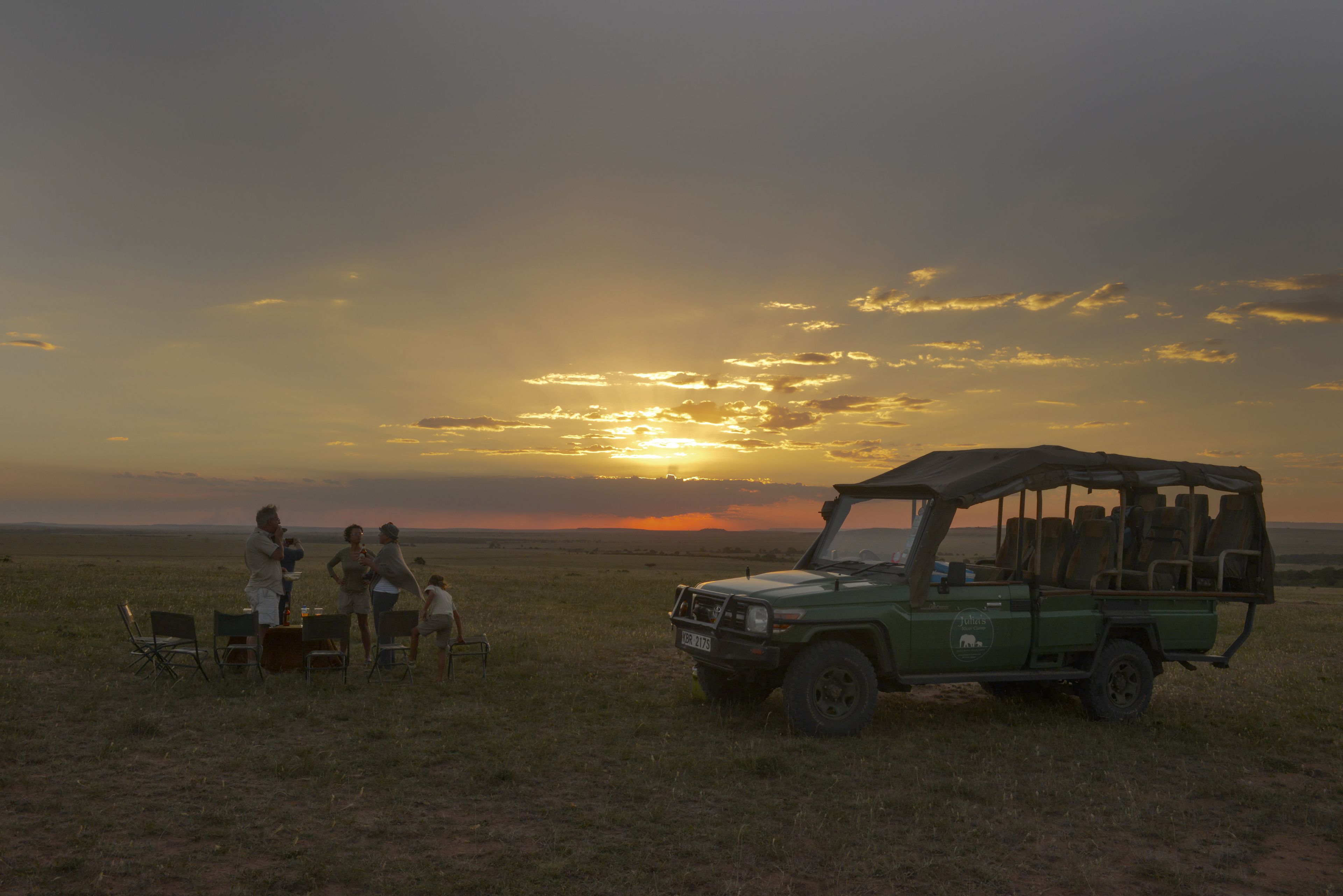 A safari vehicle parked in a grassy field with a sunset in the background.
