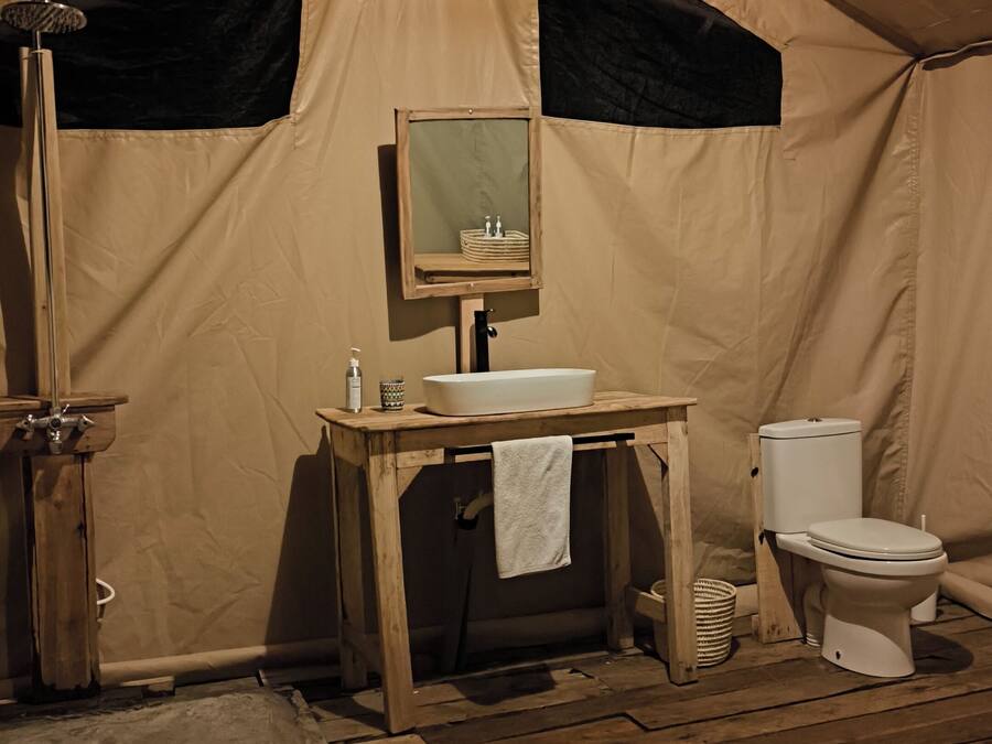 Una tenda con pavimento in legno, lavandino, toilette e specchio.