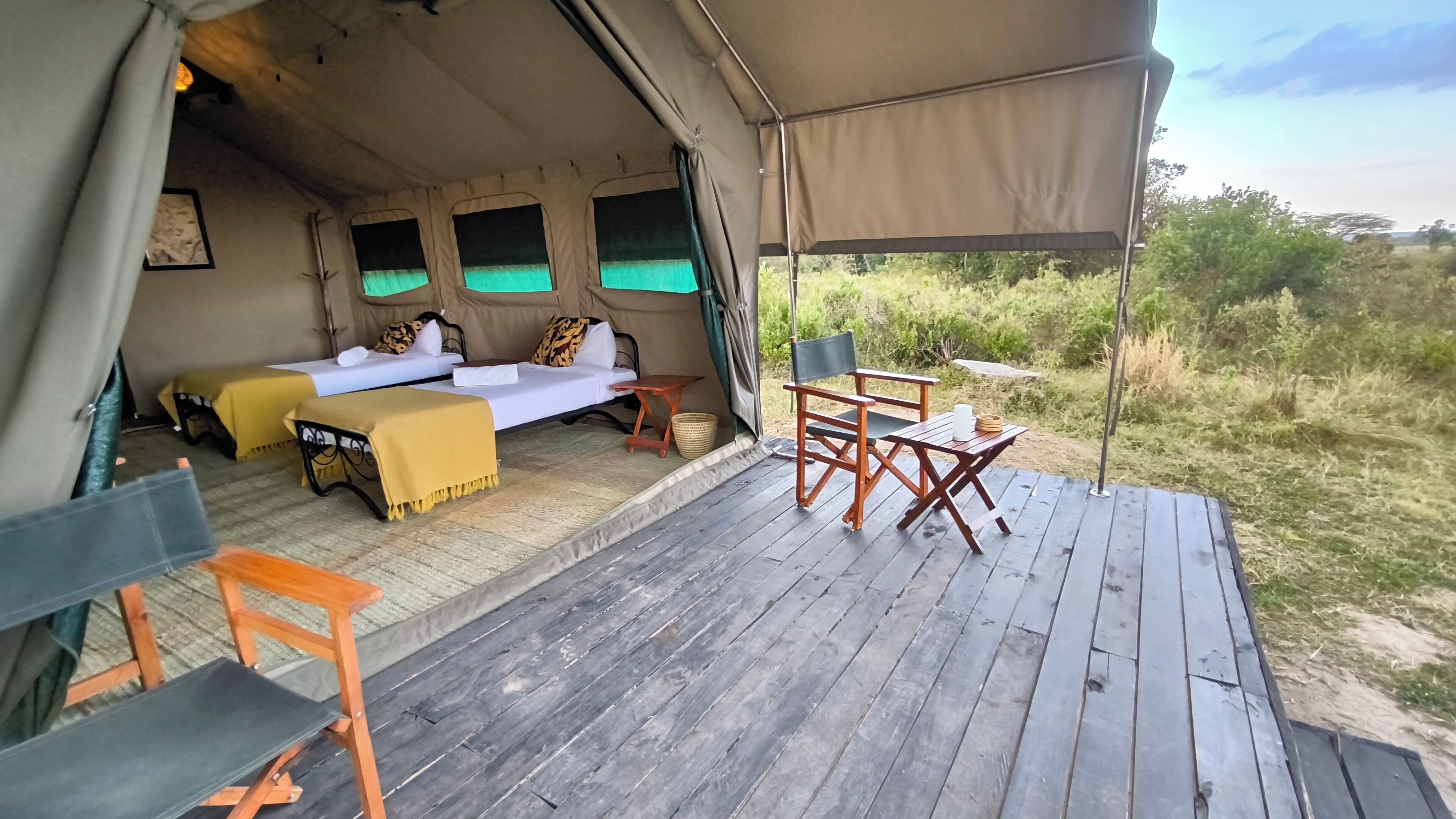 Una carpa con dos camas, una mesa y sillas sobre una terraza de madera.
