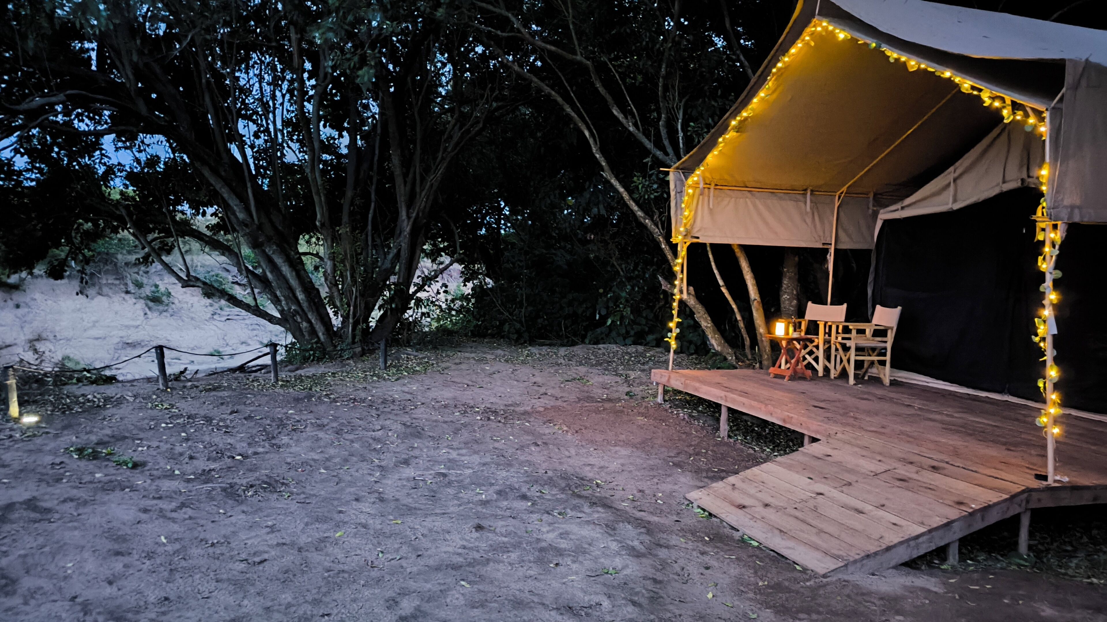 A tent with a wooden deck and seating area, surrounded by trees and a dirt path.