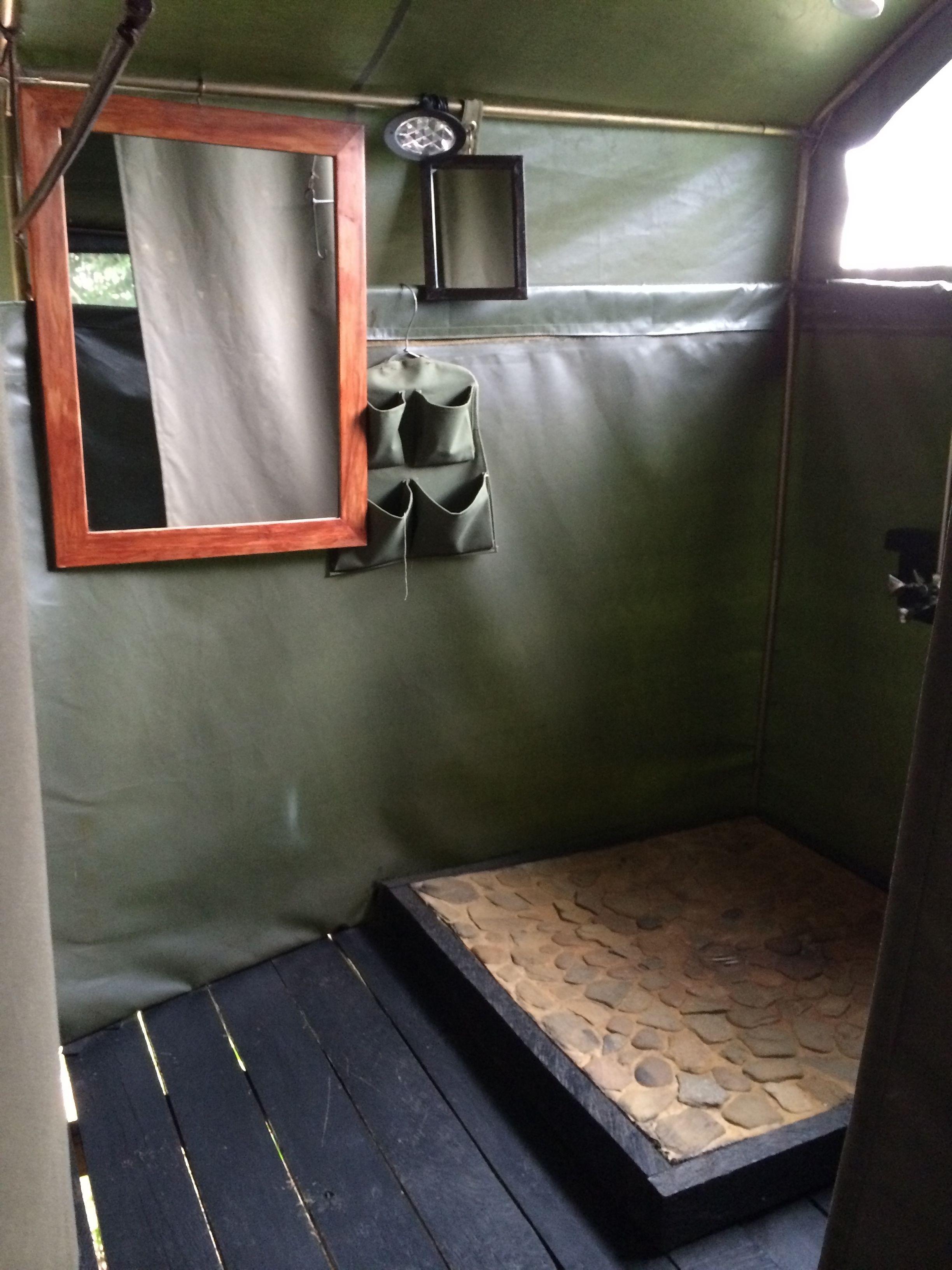 A small, enclosed space with a mirror, a small shelf, and a step leading to a stone-tiled floor.
