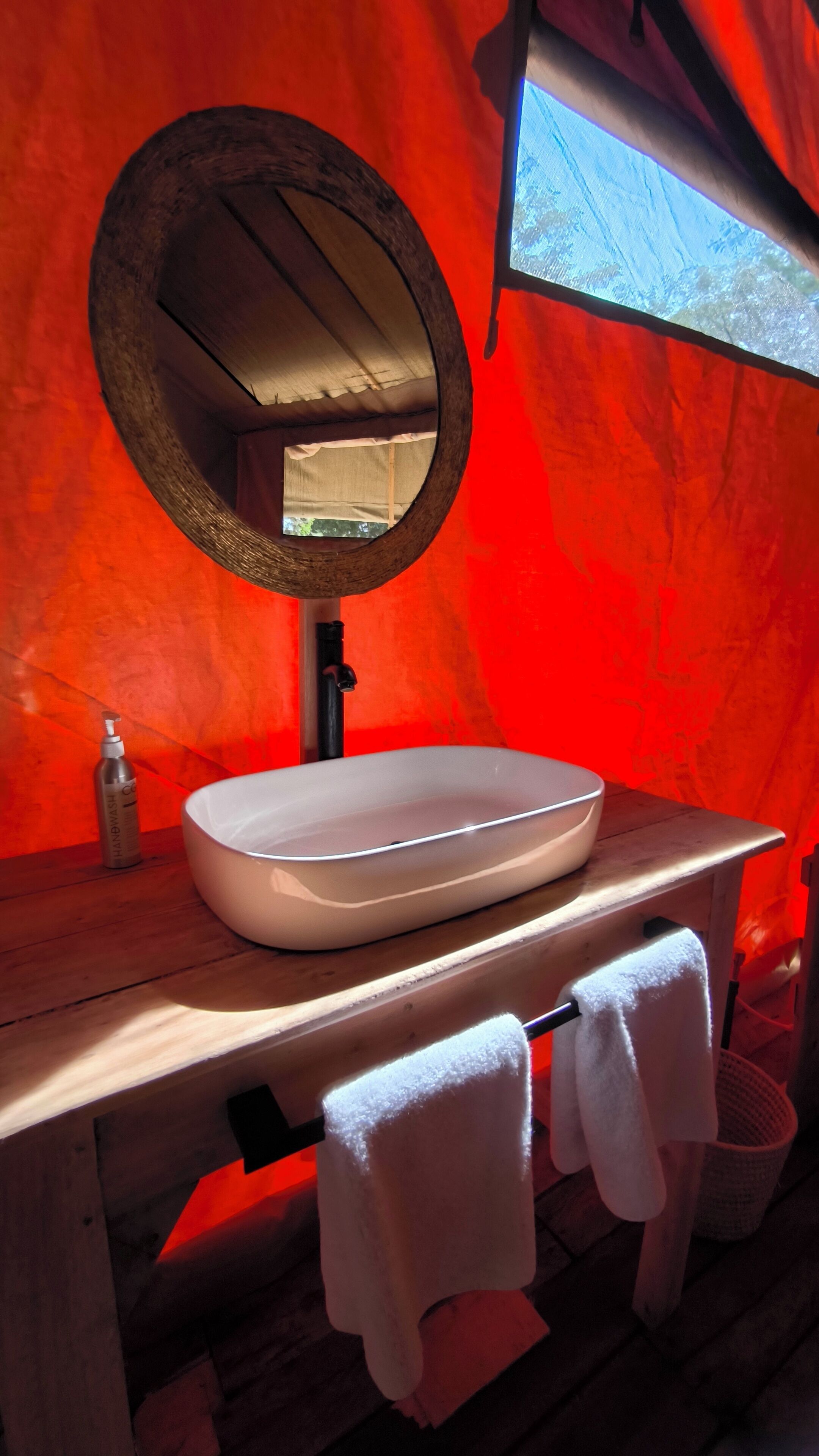 A bathroom with a wooden vanity, a white sink, a round mirror, and a window above the sink.