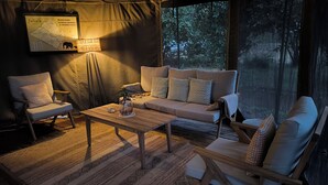 Un espace sous tente, chaleureux et bien éclairé, avec un canapé, des fauteuils et une table en bois. On peut voir une carte et une lampe sur le mur.