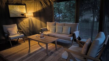Un espacio amigable y bien iluminado con carpas, un sofá, sillas y una mesa de madera. Se ve un mapa y una lámpara en la pared.
