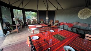 Un espace de restauration en plein air, avec des tables et des chaises en bois, abrité par une grande tente.