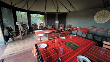 Un espacio de comedor al aire libre con mesas y sillas de madera, cubierto por una gran carpa.