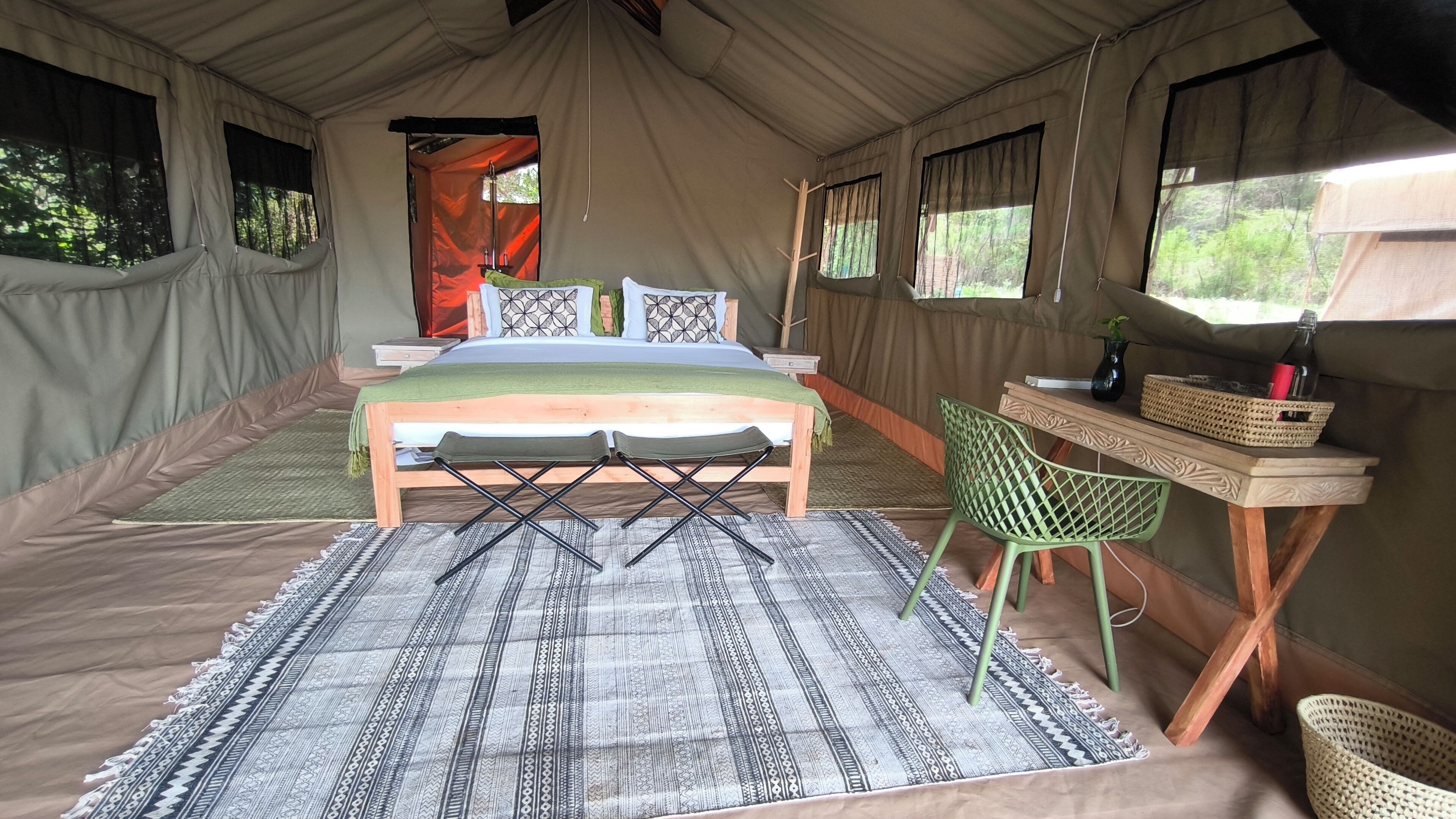 A tented room with a bed, a desk, a chair, and a patterned rug.
