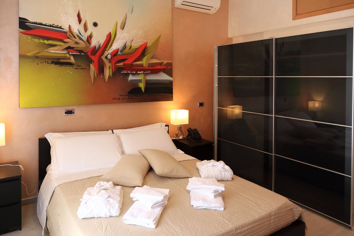 A hotel room with a bed, a nightstand, a lamp, a painting, and a sliding door.