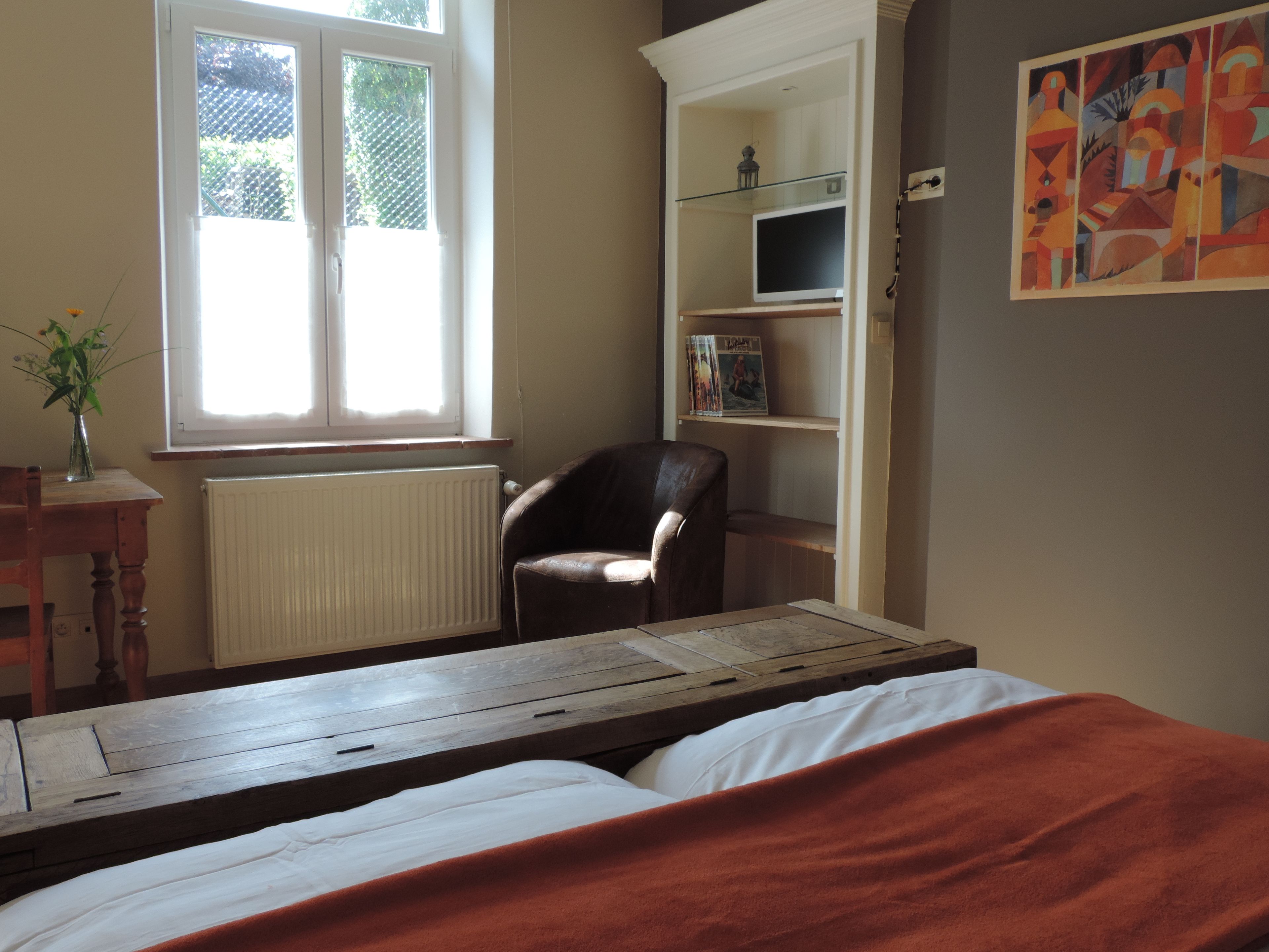 A bedroom with a bed, a chair, a radiator, a window, and a bookshelf.