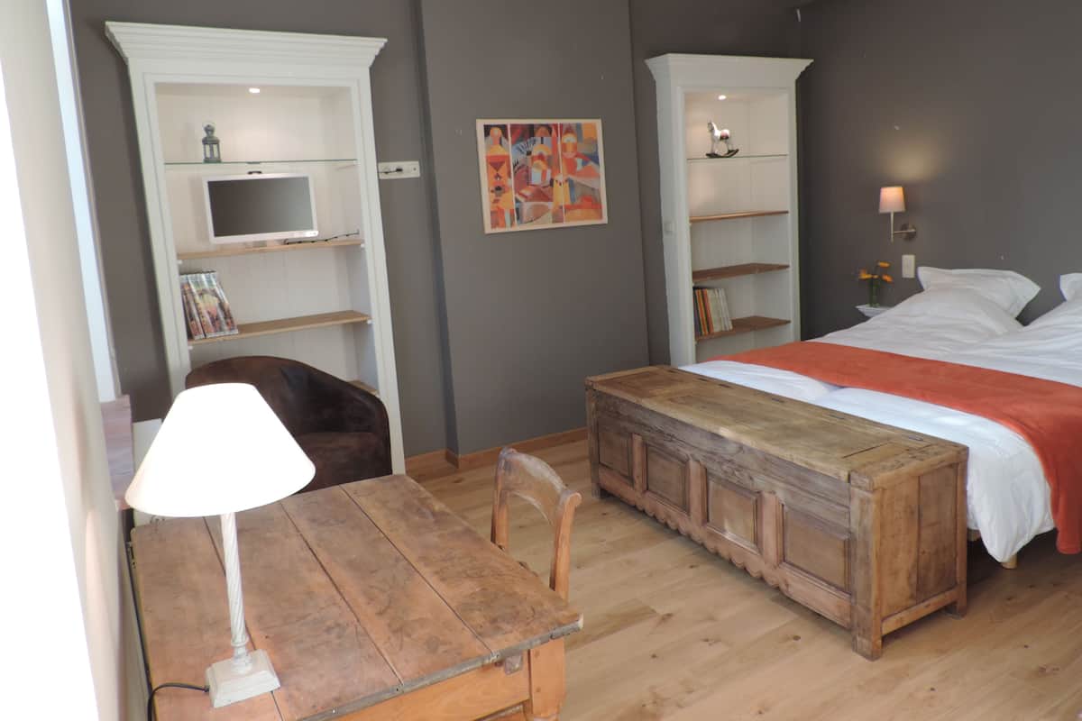 Et soveværelse med seng, skrivebord med lampe, stol og indbyggede reoler med TV og bøger.