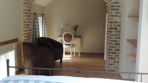 A room with a brick archway, a bed, a chair, a table with a lamp, and a hanging plant. - B&B Le Valangré (Chaumont-Gistoux)