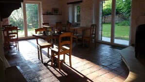 A rustic dining area with stone walls, wooden furniture, and large sliding glass doors leading to a garden. - B&B Le Valangré (Chaumont-Gistoux)