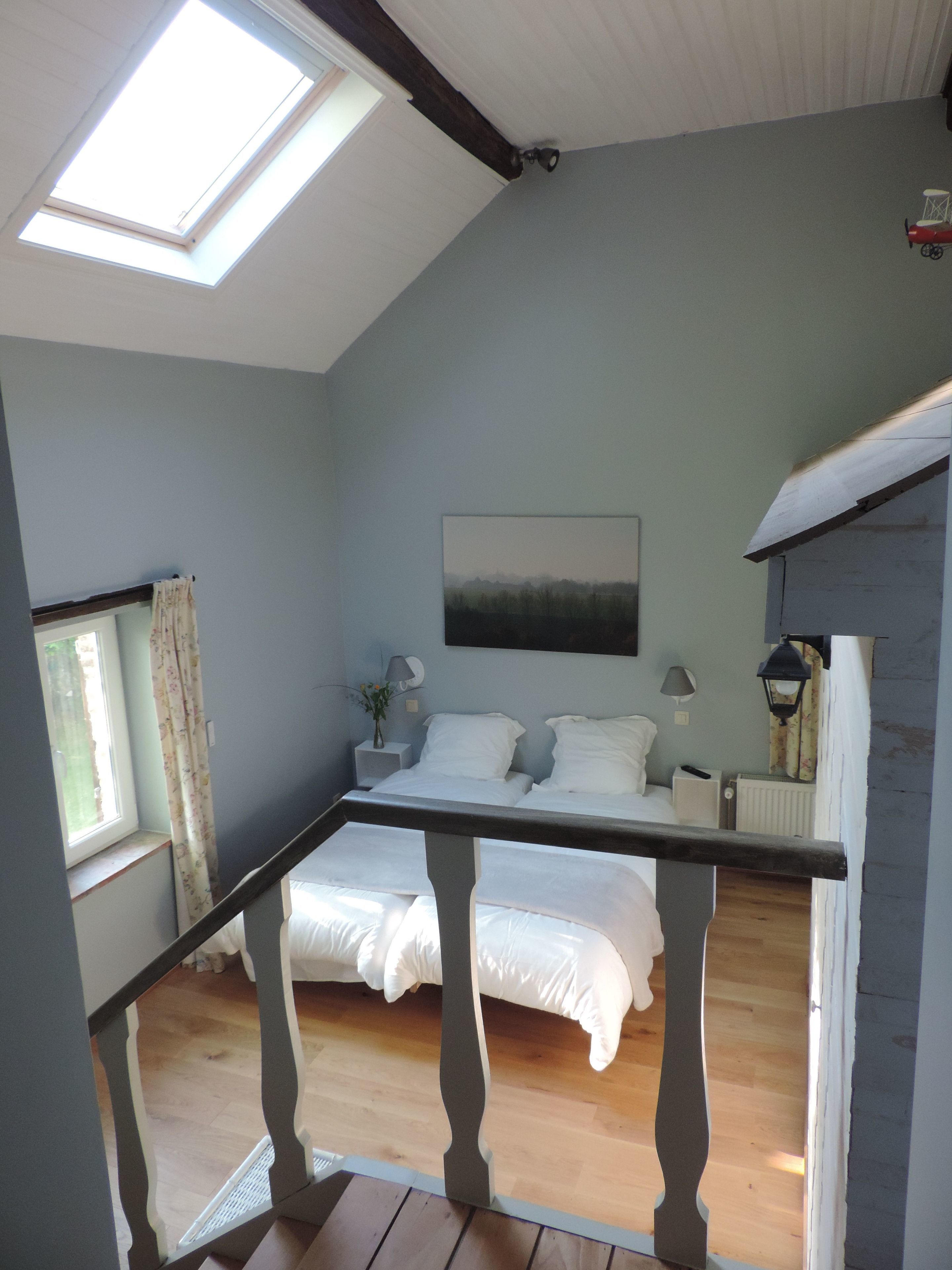 A bedroom with a skylight, a bed, a nightstand, and a window with curtains.