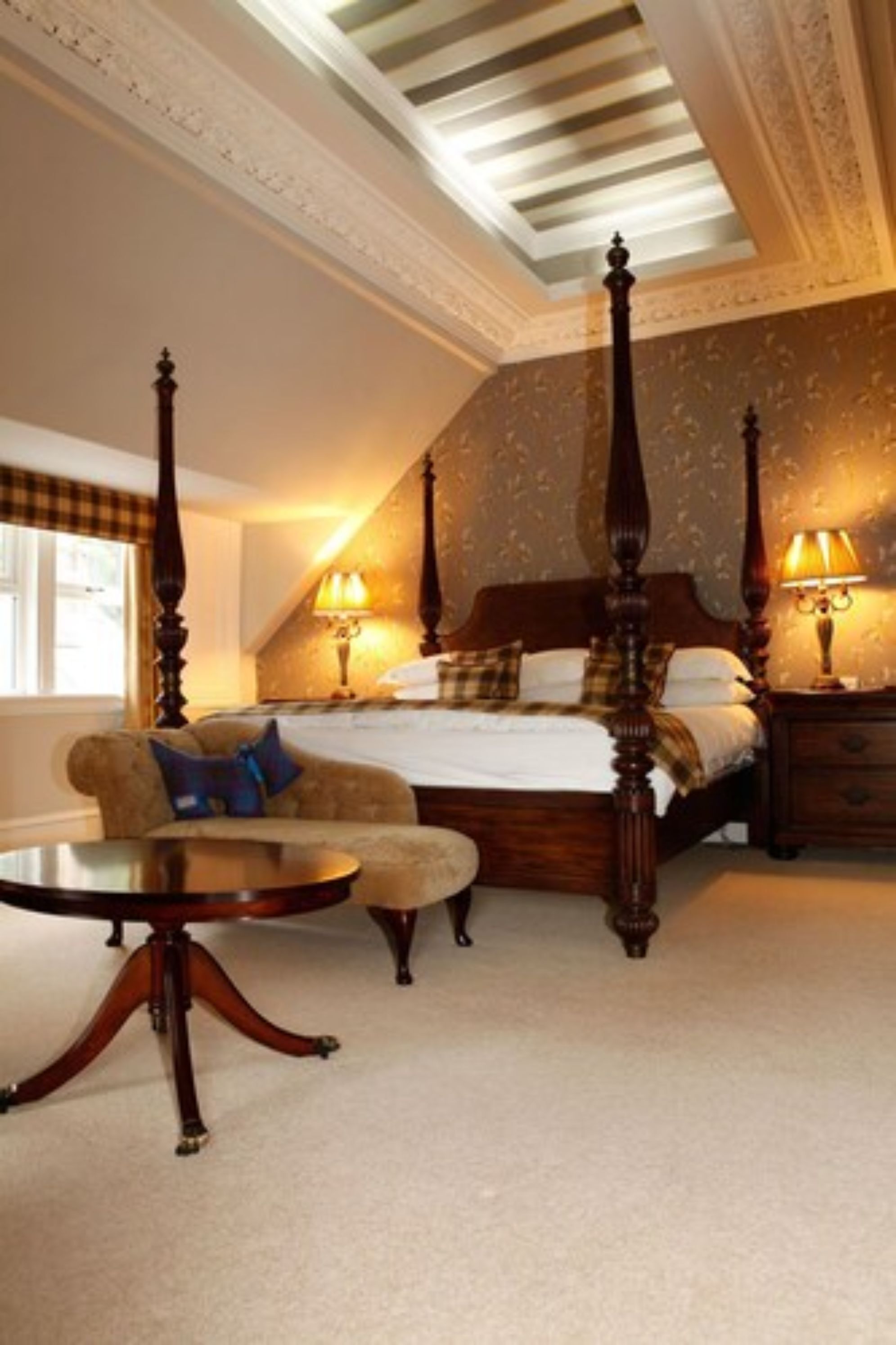 A bedroom with a four-poster bed, a sofa, a small table, and a nightstand with lamps.