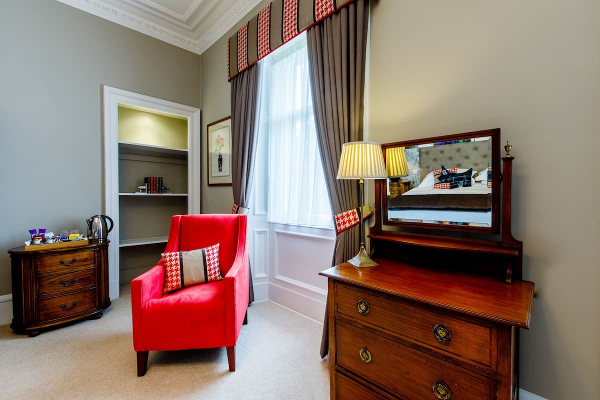 A room with a red armchair, a wooden dresser, a mirror, and a bookshelf.