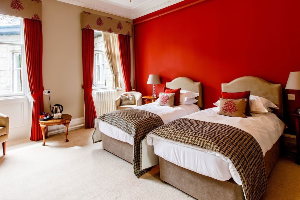 A hotel room with two beds, a chair, a small table, and a window with curtains.