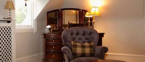 A room with a dark blue armchair, a round wooden table, and a mirror with a wooden frame.
