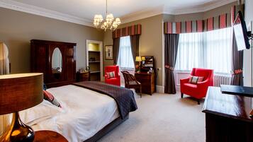 A hotel room with a large bed, a desk, a red armchair, a wooden dresser, and a mirror.
