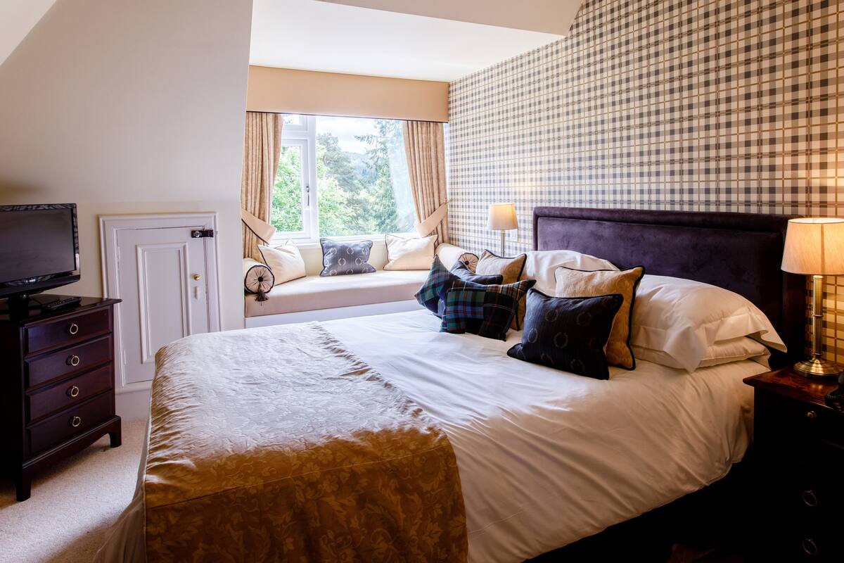 A bedroom with a bed, a television on a dresser, a window with curtains, and a checkered wall.