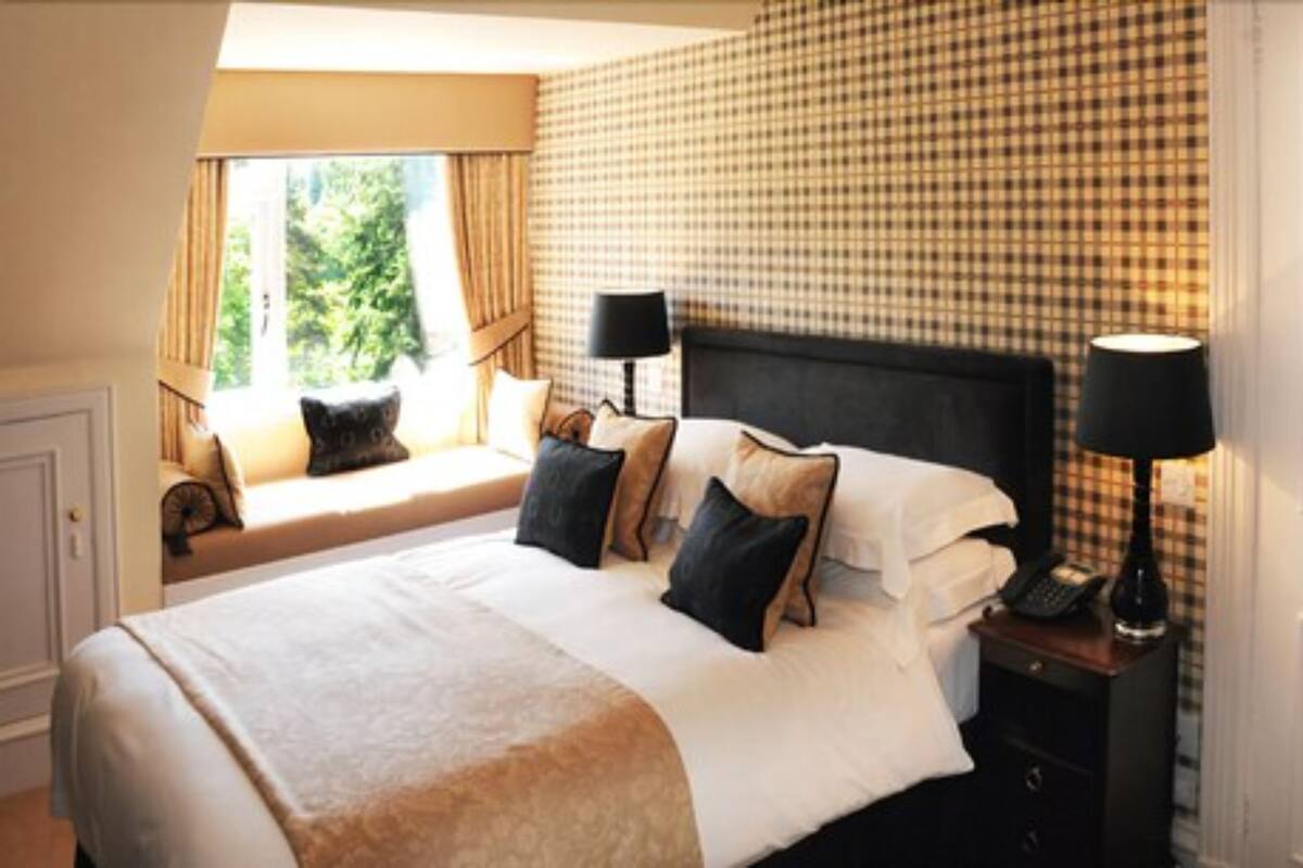 A hotel room with a large bed, two bedside tables, a window with curtains, and a checkered wall.