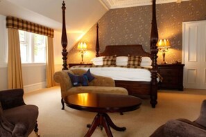 A four-poster bed with a headboard, two bedside tables with lamps, a round coffee table, and two armchairs. - Tor Na Coille Hotel & Restaurant (Banchory)