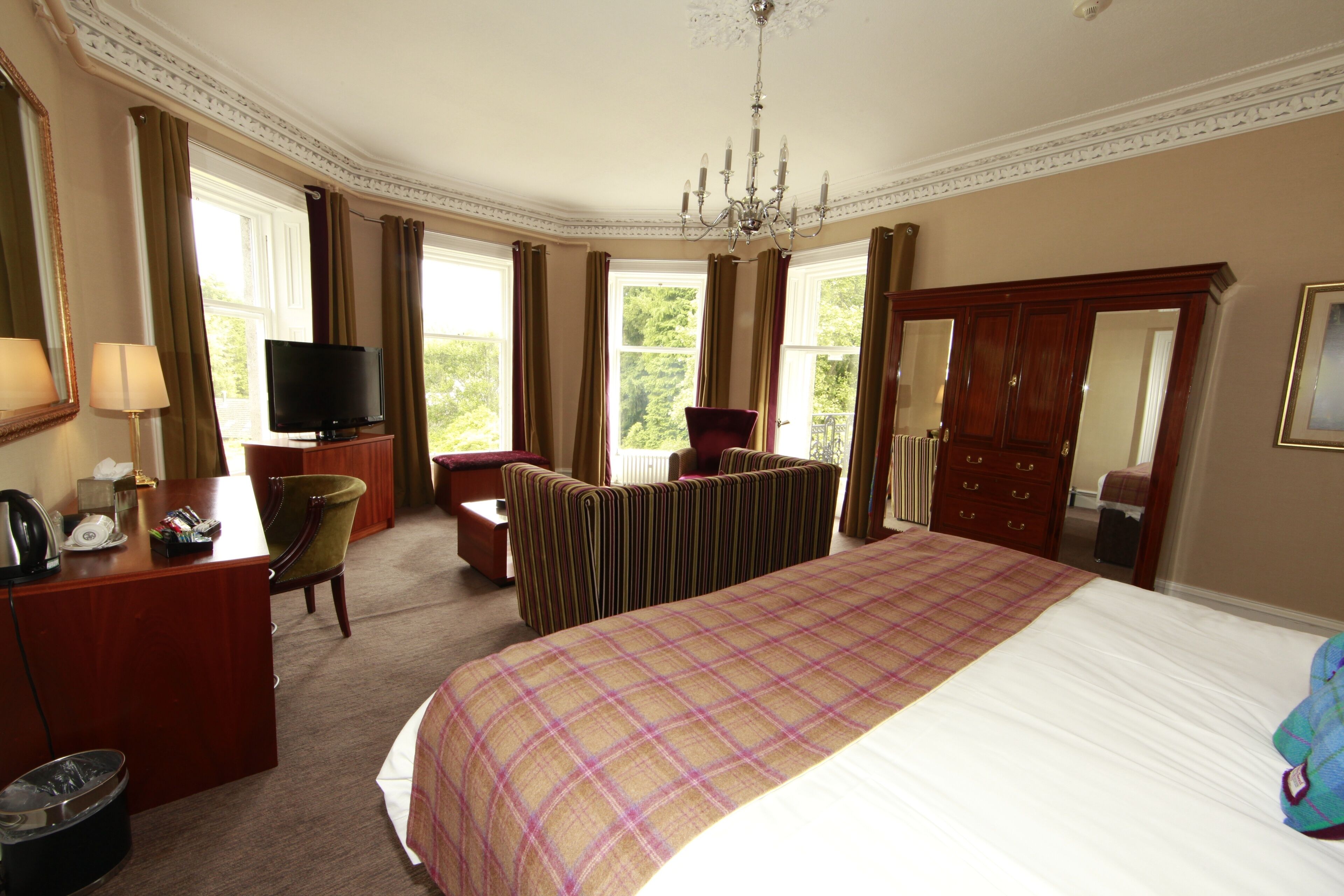 A hotel room with a large bed, a television, a desk with a telephone, and a chair.