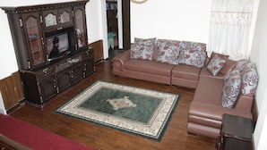 A living room with a brown sofa, patterned cushions, a wooden cabinet, and a green and white patterned rug. - Kathmandu Homestay (Kathmandu)