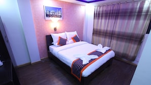 A neatly made bed with white linens and orange accents, a wall-mounted light, and a window with a plaid curtain. - Kathmandu Homestay (Kathmandu)