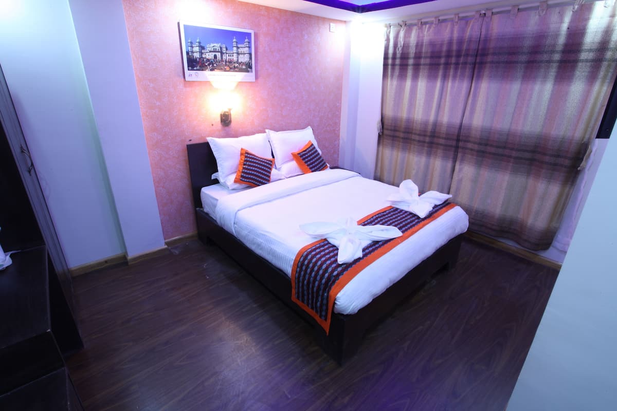 A neatly made bed with white linens and orange accents, a wall-mounted light, and a window with a plaid curtain.